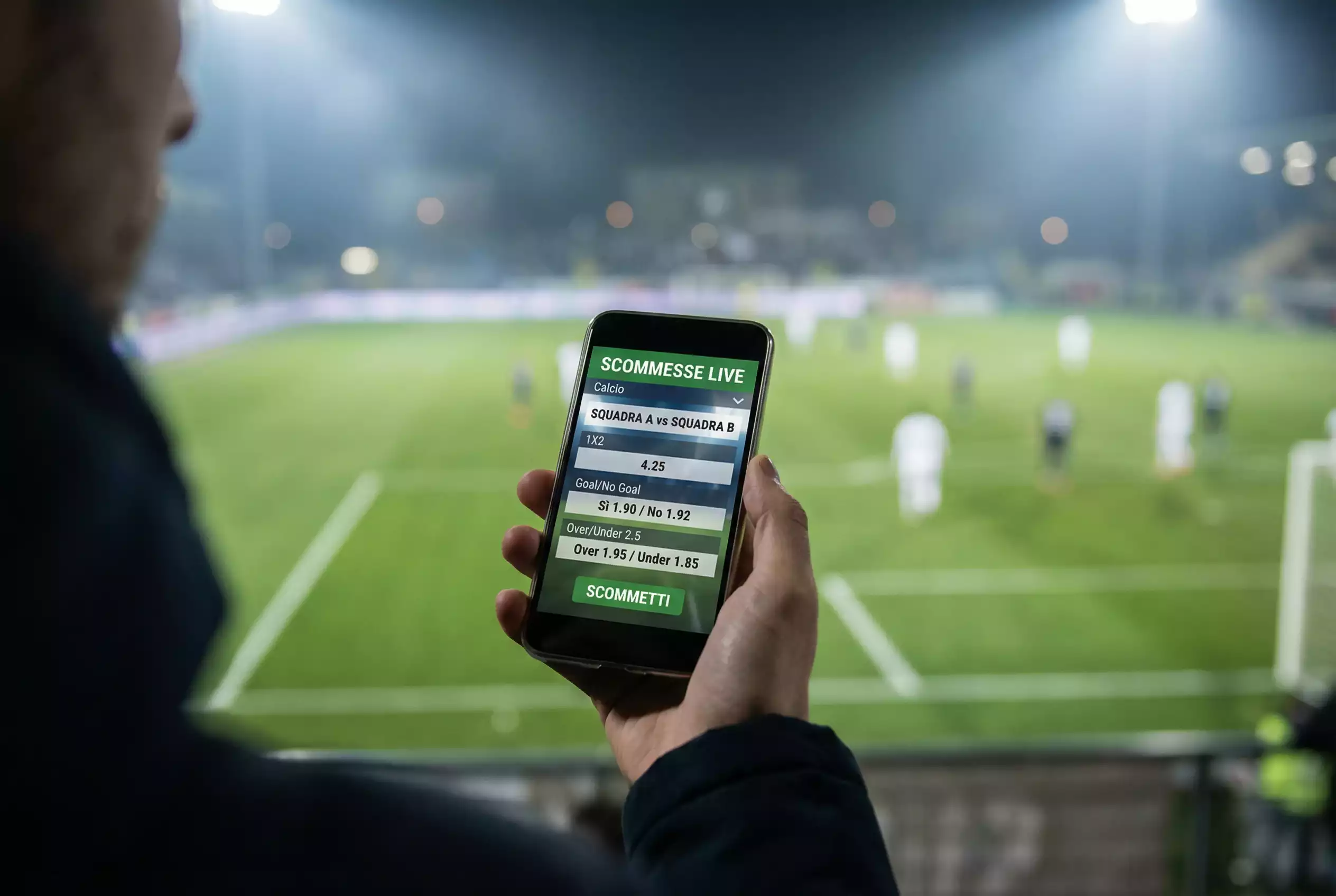 Smartphone con scommesse live durante una partita di calcio visibile sullo sfondo